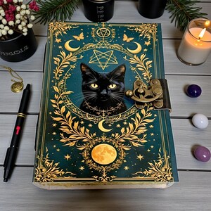 May include: A teal and gold journal featuring a black cat illustration. The cover has a decorative design with moons, stars, and a pentagram. It has a clasp closure and a full moon graphic at the bottom.