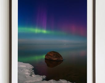Puede incluir: Impresión enmarcada de un paisaje nocturno con la aurora boreal. El cielo transita del azul profundo al púrpura y al verde, con la aurora reflejada en el agua en calma. Una gran roca se encuentra en el agua y hielo bordea la orilla.