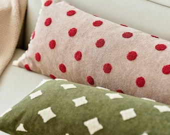 May include: A rectangular beige pillow featuring a textured red polka dot pattern and a white fringed edge, positioned behind a rectangular olive green pillow with a white embroidered diamond pattern and a white fringed edge.
