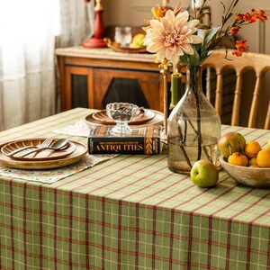 May include: A dining table set with a green and red plaid tablecloth. The table is set with wooden plates, silverware, a glass vase with flowers, and a bowl of fruit. A book titled "ANTIQUITIES" is also on the table.