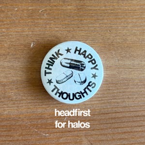 May include: A round, light blue button with the words "THINK HAPPY THOUGHTS" encircling three pill illustrations. The text "headfirst for halos" is below the button.