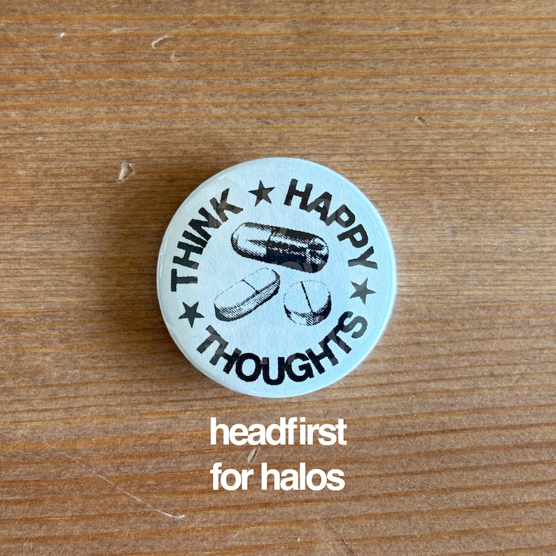 May include: A round, light blue button with the words "THINK HAPPY THOUGHTS" encircling three pill illustrations. The text "headfirst for halos" is below the button.