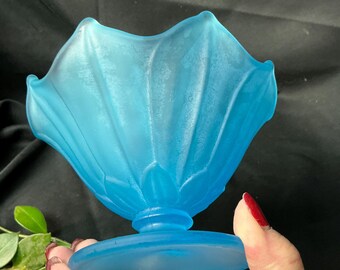 May include: A bright blue frosted glass bowl with a scalloped, petal-like rim and a fluted body. The bowl features a circular pedestal base and a smooth, matte texture throughout, showcasing a vibrant, semi-translucent finish in a distinct flower shape.