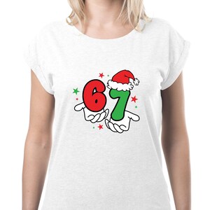 May include: White t-shirt with a festive graphic. The design features the numbers "6" and "7" in red and green, respectively, held by cartoon hands. The number "7" is wearing a Santa hat, with red and green stars.