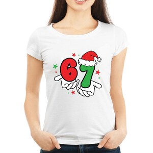 May include: White t-shirt featuring a festive graphic with the numbers 6 and 7. The number 7 is wearing a Santa hat. The numbers are held by cartoon hands, with red and green stars scattered around the design. A fun, holiday-themed tee.