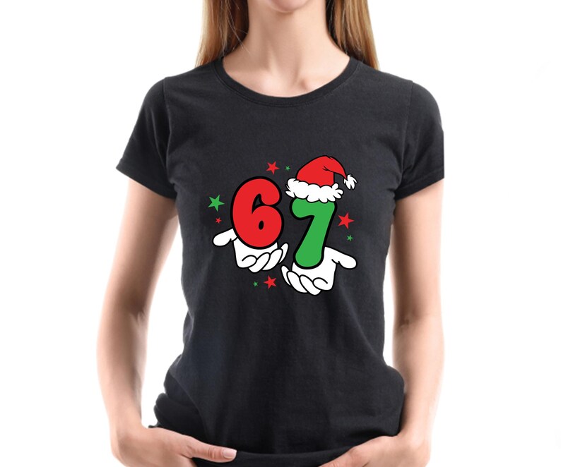 May include: Black t-shirt featuring the numbers 6 and 7 in red and green, held by cartoon hands. The number 7 is wearing a Santa hat. Red and green stars are scattered around the numbers, creating a festive design.