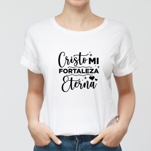 Może przedstawiać: Biała koszulka z napisem "Cristo MI Fortaleza Eterna" w czarnym skrypcie. Koszulka ma kr&oacute;tkie rękawy i okrągły dekolt. Tekst zawiera ozdobne gwiazdki i serca.