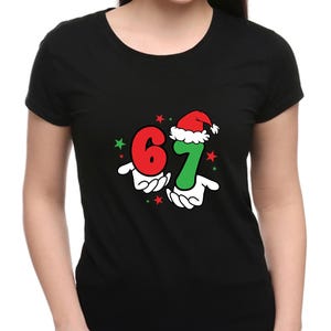 May include: Black t-shirt featuring the numbers "6" and "7" in red and green, with a Santa hat on the "7". The numbers are held by cartoon hands, with red and green stars. A festive holiday design.