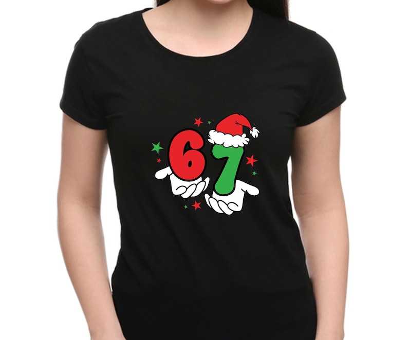 May include: Black t-shirt featuring the numbers "6" and "7" in red and green, with a Santa hat on the "7". The numbers are held by cartoon hands, with red and green stars. A festive holiday design.