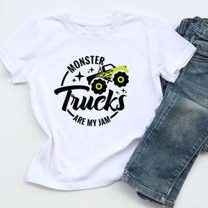 May include: White t-shirt with a black and neon green graphic of a monster truck and the text "Monster Trucks are my Jam." The shirt is paired with blue denim jeans.
