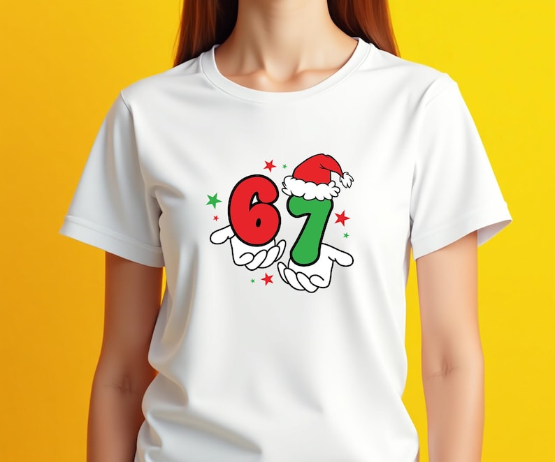 May include: White t-shirt featuring a festive design with the numbers "6" and "7" in red and green, respectively. The number "7" is adorned with a Santa hat. The design includes red and green stars, and the numbers are held by cartoon hands.