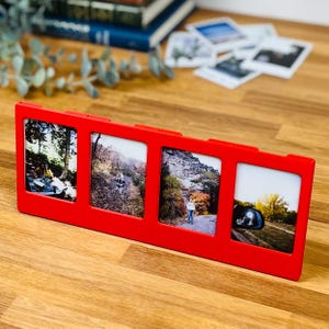 May include: A bright red rectangular plastic photo frame featuring four vertical slots for displaying individual pictures. The frame has a smooth, solid-colored finish and is designed to hold four separate photographs in a side-by-side horizontal arrangement.
