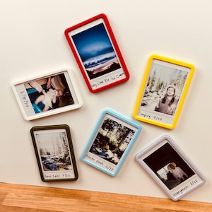May include: Six rectangular magnetic photo frames in red, yellow, light blue, white, olive green, and light gray. Each frame holds a small photograph with handwritten text at the bottom, including labels like Key Lime Pie Ice Cream, Camping 7/22, Provo Falls 7/22, Beaver Ponds 6/22, Honeymoon 6/22, and 6/30/24.