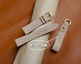 Peut inclure: Un bracelet de montre en cuir beige clair avec une boucle dorée et un porte-clés assorti. Le bracelet de montre comporte plusieurs trous pour le réglage. Le porte-clés a un anneau doré et une fermeture à bouton-pression. Le texte "GIFT-KEY CHAIN" est dans l'image.