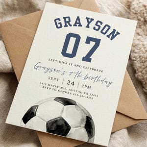 May include: A birthday invitation with a soccer theme, featuring the name "Grayson" and the number "07" in navy blue. The invitation includes the text "Let's kick it and celebrate" and "Grayson's 7th birthday". A watercolor soccer ball is at the bottom.