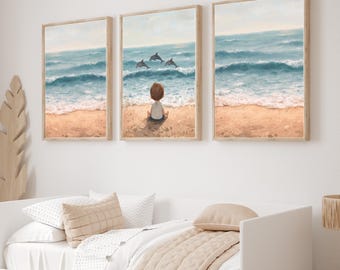Puede incluir: Tres impresiones enmarcadas que representan una escena de playa con un niño y delfines. Las impresiones tienen un marco de madera clara y están colgadas sobre una cama blanca con ropa de cama beige. Un caballito de madera y una cesta de mimbre también están en la habitación.