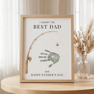 May include: A framed print with the text "I CAUGHT THE BEST DAD" above a watercolor illustration of a fishing rod and a handprint fish. The words "HAPPY FATHER'S DAY" are below the illustration.