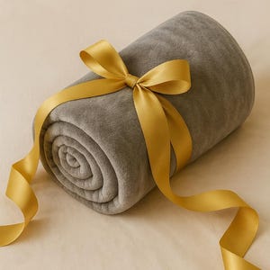May include: A rolled-up gray blanket tied with a gold satin ribbon and bow. The blanket is soft and plush, and the ribbon adds a touch of elegance. Perfect for gifting or personal use.