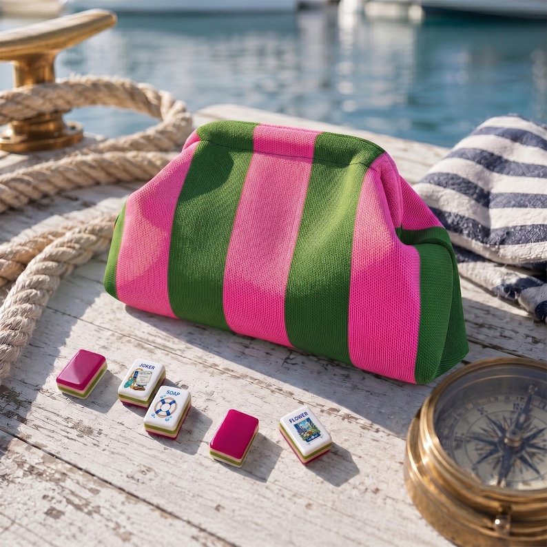 May include: A fabric pouch featuring vertical stripes in bright pink and olive green. Arranged in front are four small rectangular tiles, including one labeled Joker, one labeled Soap, and one labeled Flower, alongside a brass nautical compass.