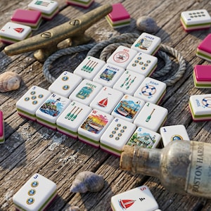May include: A set of nautical-themed mahjong tiles featuring illustrations of sailboats, lighthouses, anchors, and oars, arranged on a weathered wooden surface alongside a metal boat cleat, a coiled rope, seashells, and a glass bottle labeled Boston Harbor.