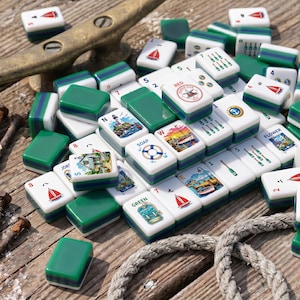 May include: A collection of white and green mahjong tiles featuring nautical illustrations, including sailboats, lighthouses, life preservers, and bottles. The tiles display various numbers, letters, and the text RED HARBOR CLUB, SOAP, and GREEN.