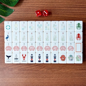 May include: A set of white Mahjong tiles with various symbols and numbers, including octopuses, flowers, and lighthouses. Two red dice are also present. The tiles are arranged on a wooden surface.