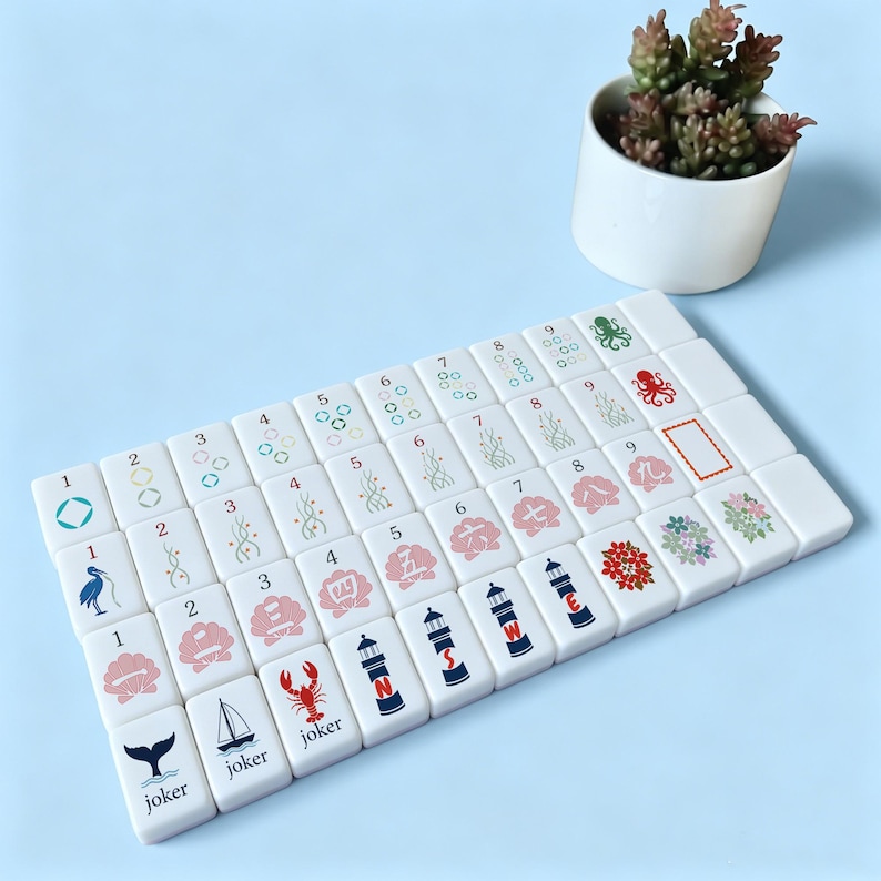 May include: A set of white Mahjong tiles with various colorful symbols and numbers. The tiles feature images of a whale tail, a sailboat, a lobster, and a lighthouse. The numbers and symbols are in red, green, and blue.