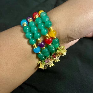 May include: A collection of beaded bracelets featuring green, yellow, red, purple, and blue beads. The bracelets have gold-colored turtle charms. The beads are strung together with gold-colored spacers.