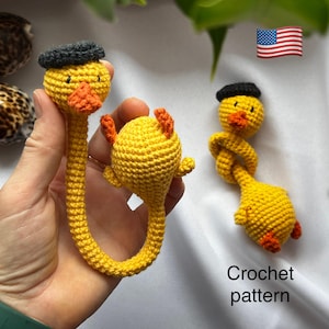 以下が含まれることがあります： オレンジ色のくちばしと足、黒いベレー帽をかぶった、かぎ針編みの黄色のカモのブックマーク。ブックマークは手作りで、詳細なかぎ針編みのパターンが特徴です。「Crochet pattern」というテキストが画像に表示されています。