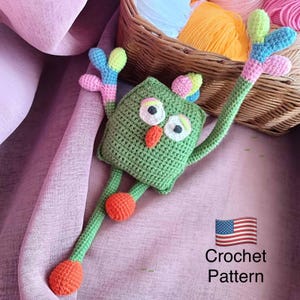 May include: A green crochet owl-like creature with large white eyes, an orange beak, and orange feet. The creature has long arms with colorful accents. The image includes the text "Crochet Pattern" and an American flag.