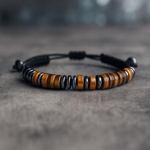 May include: A beaded bracelet featuring alternating sections of brown tiger eye stones and dark gray metal beads. The bracelet is strung on a black cord with an adjustable sliding knot closure. A stylish accessory.