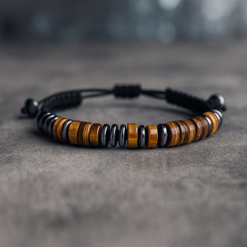 May include: A bracelet with alternating sections of brown tiger eye stones and dark grey metal beads. The bracelet is strung on a black cord with an adjustable sliding knot closure. A stylish accessory.