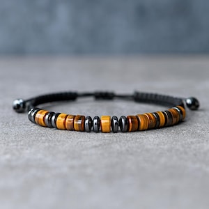 May include: A bracelet with a black cord and a sliding knot closure. The bracelet features a series of brown, yellow, and black beads. The beads are round and of varying sizes. The bracelet is designed to be adjustable.