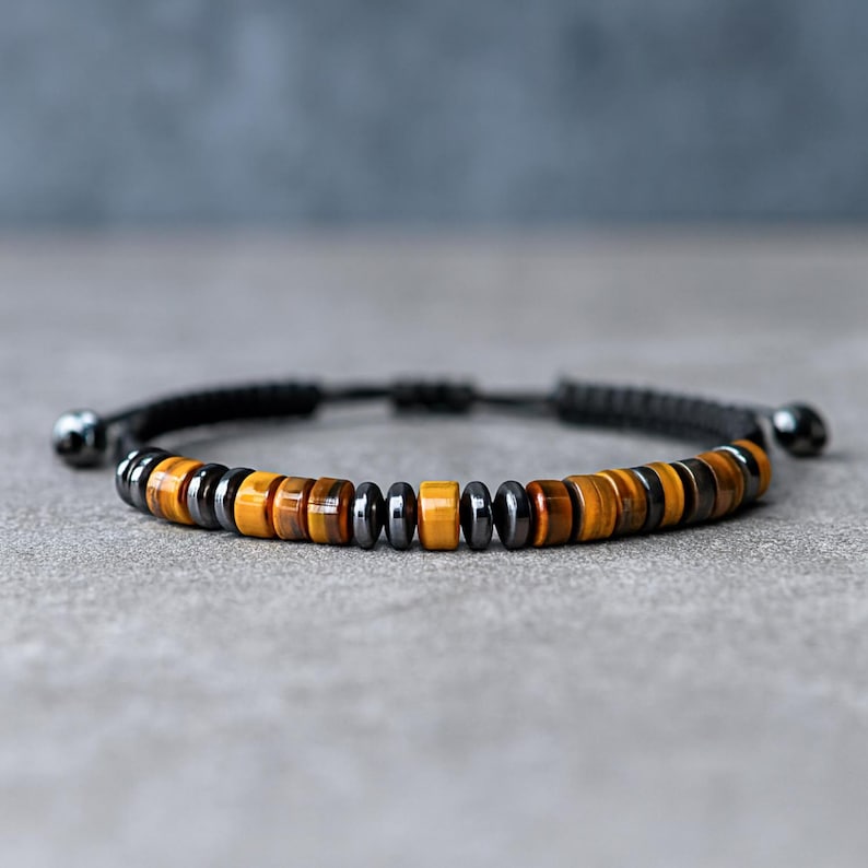 May include: A bracelet with a black cord and a sliding knot closure. The bracelet features a series of brown, yellow, and black beads. The beads are round and of varying sizes. The bracelet is designed to be adjustable.