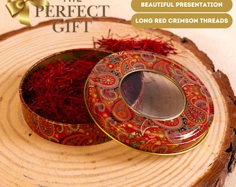 Könnte beinhalten: Eine runde, rote Dose mit Paisley-Muster, gefüllt mit langen, karmesinroten Fäden. Der Deckel hat ein klares Fenster. Der Text "THE PERFECT GIFT" ist sichtbar. Die Dose steht auf einer Holzoberfläche.