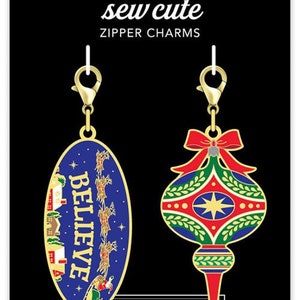 May include: Two gold zipper charms with a Christmas theme. One charm is a blue oval with the word "BELIEVE" in white letters and a scene of Santa's sleigh flying through the night sky. The other charm is a red and green ornament with a gold star and a red bow.
