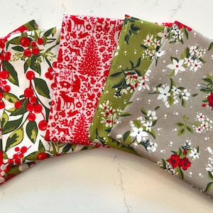 May include: A collection of folded fabric squares with festive holiday patterns. Designs include red berries, Christmas trees, and floral arrangements in red, green, and white on a neutral background. Ideal for seasonal crafts.