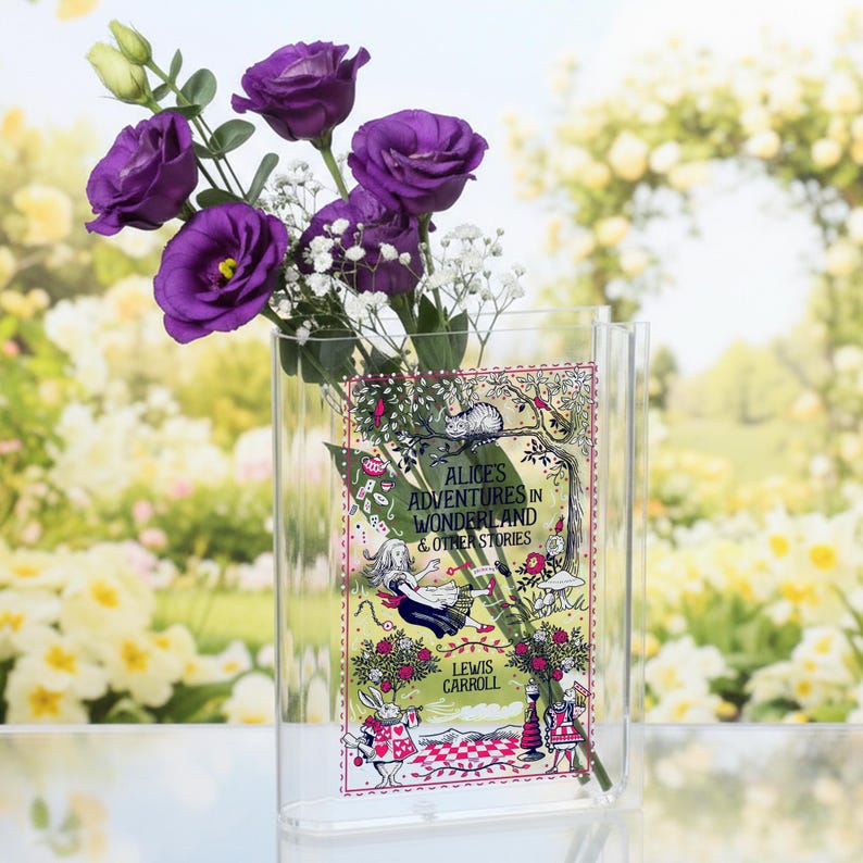 May include: A clear acrylic vase with a colorful illustration of "Alice's Adventures in Wonderland" by Lewis Carroll. The vase holds a bouquet of vibrant purple flowers and white filler flowers. The background is a soft focus of yellow and green.