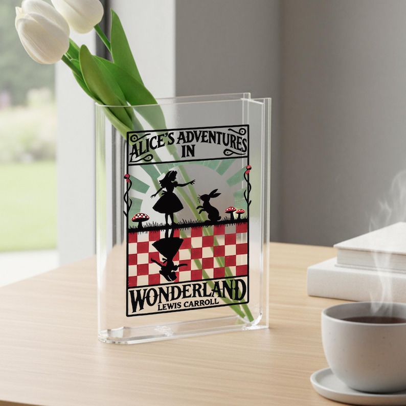 May include: Clear acrylic vase with the text "Alice's Adventures in Wonderland" and a silhouette of Alice and the rabbit. The vase holds white tulips and is on a wooden table.