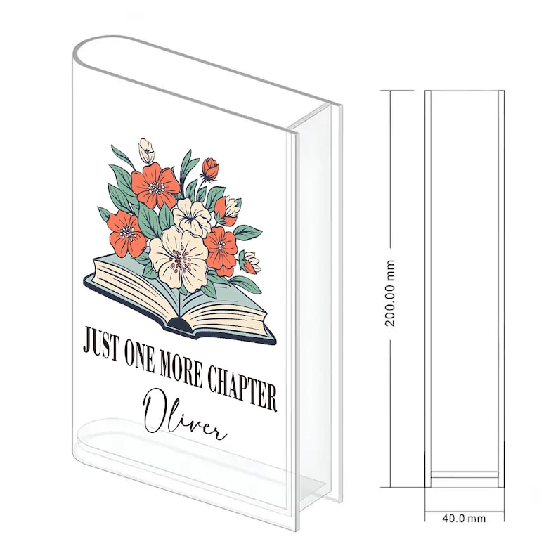 May include: Clear acrylic book-shaped display stand. The front features an open book illustration with a floral bouquet in orange, white, and teal. Text reads "JUST ONE MORE CHAPTER Oliver." The stand is 20 cm tall and 4 cm wide.