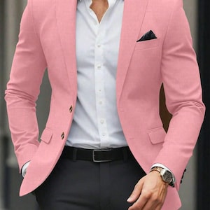 Może przedstawiać: Jasnoróżowa marynarka ze złotymi guzikami, połączona z białą koszulą, czarnymi spodniami i czarnym paskiem. Czarna poszetka jest widoczna w kieszeni piersi marynarki. Zegarek na rękę jest na nadgarstku.