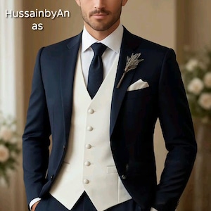 Puede incluir: Un traje azul marino con chaleco blanco, camisa blanca y corbata azul marino. Un pequeño ojal floral y un pañuelo blanco añaden detalles. El texto "HussainbyAn as" es visible en la imagen.