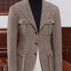 Puede incluir: Blazer marrón con diseño de espiga, cuatro bolsillos delanteros y botones marrones. El blazer se lleva sobre un cuello alto negro y pantalones blancos. El texto "HussainbyAnas" es visible en la parte superior.