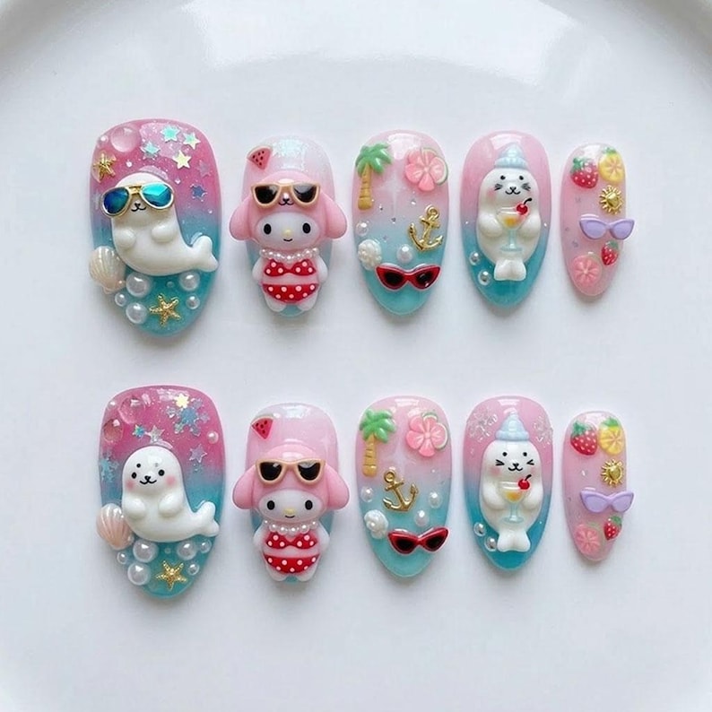 May include: A set of ten artificial nails with a summer theme. Each nail features a different design, including seals, My Melody characters, palm trees, anchors, sunglasses, and fruit. The nails are painted in shades of pink, blue, and white, with glitter accents.