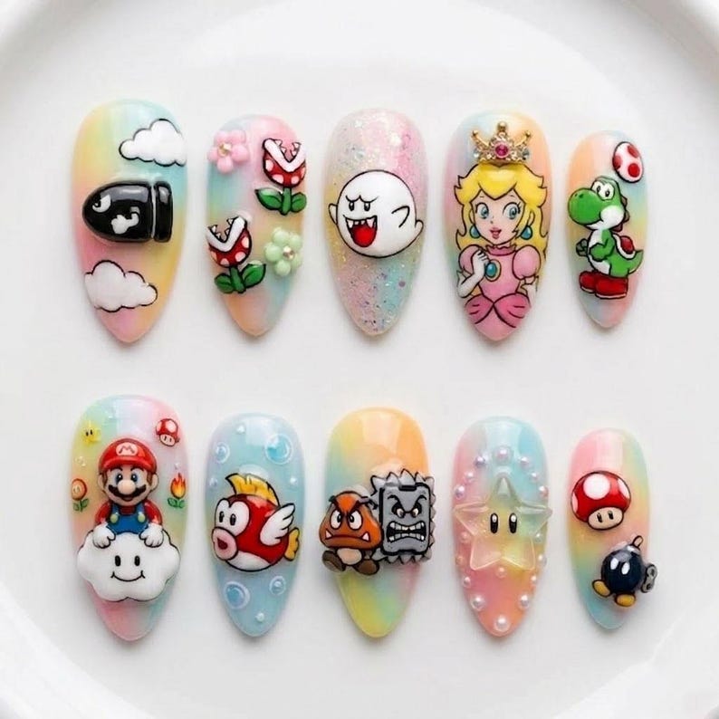 May include: A set of ten almond-shaped press-on nails featuring a pastel rainbow gradient base. The designs include 3D and flat illustrations of Mario characters such as Princess Peach, Mario, Yoshi, Boo, Goomba, Piranha Plants, and various game icons.