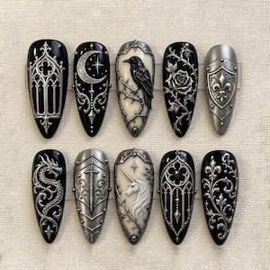 May include: A set of ten almond-shaped press-on nails featuring intricate 3D silver metallic reliefs on black and cream backgrounds. Designs include a gothic arch, crescent moon, raven, rose, shield, dragon, sword, unicorn, and floral filigree.