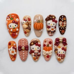 Può includere: Un set di dieci unghie finte con decorazioni autunnali in 3D. I design includono personaggi Hello Kitty in costume da zucca e maglione, zucche, ghiande, fantasmi, cuori a quadri, texture a maglia intrecciata, fiocchi e foglie d'acero.