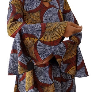 Könnte beinhalten: Ein langärmliges Kleid mit Schlüsselloch-Ausschnitt und ausgestellten Ärmeln. Das Kleid hat ein sich wiederholendes fächerartiges Muster in Rot-, Gelb- und Blautönen auf dunklem Hintergrund. Das Kleid ist aus fließendem Stoff.