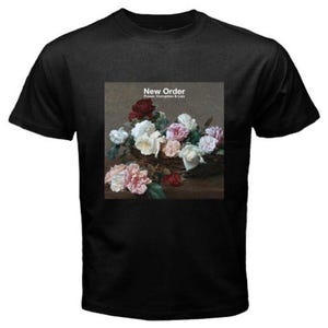 May include: Black t-shirt with a floral still life design and the text "New Order, Power, Corruption & Lies." The graphic shows a basket of white, pink, and red roses. The shirt has a crew neck.