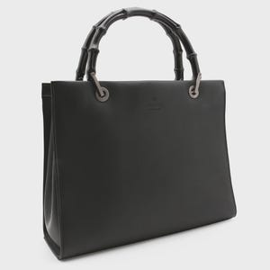 May include: Black leather tote bag with bamboo handles. The bag features a rectangular shape with a structured design. The handles are dark brown and curved. The bag has a silver-tone hardware and the brand name is visible.